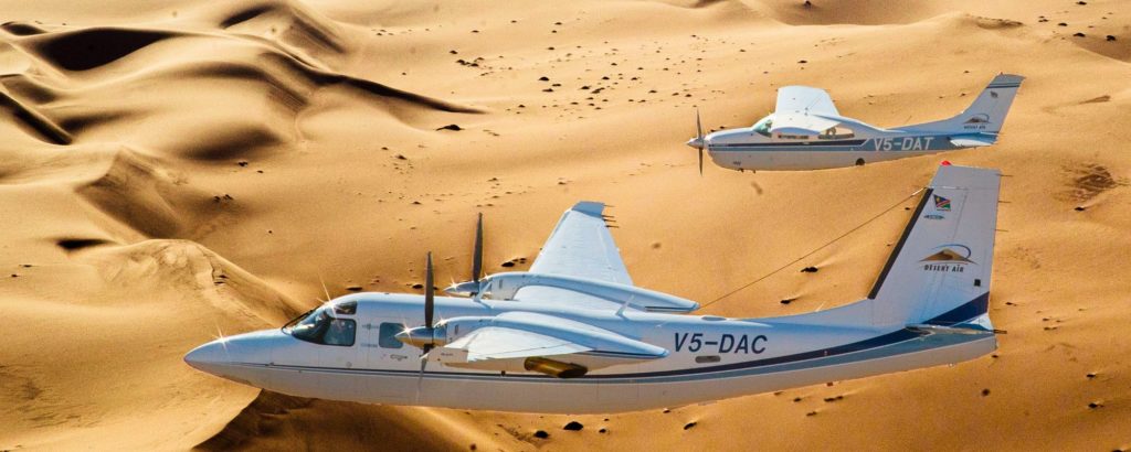 Zwei Flugzeuge - Aero Commander & Cessna 210 gemeinsam vor dem Hintergrund der Dünenlandschaft des Sossusvlei