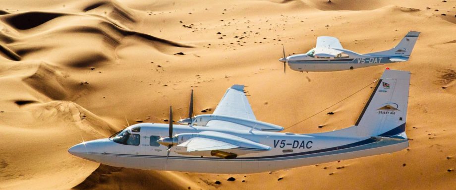 Zwei Flugzeuge - Aero Commander & Cessna 210 gemeinsam vor dem Hintergrund der Dünenlandschaft des Sossusvlei