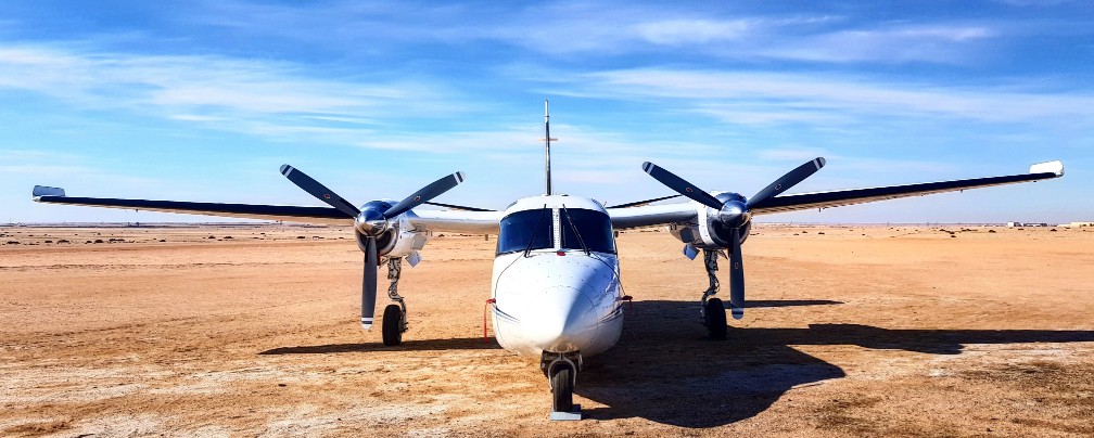 Aero Commander von vorne mitten in flacher Sandwüste Namibias vor blauem Himmel